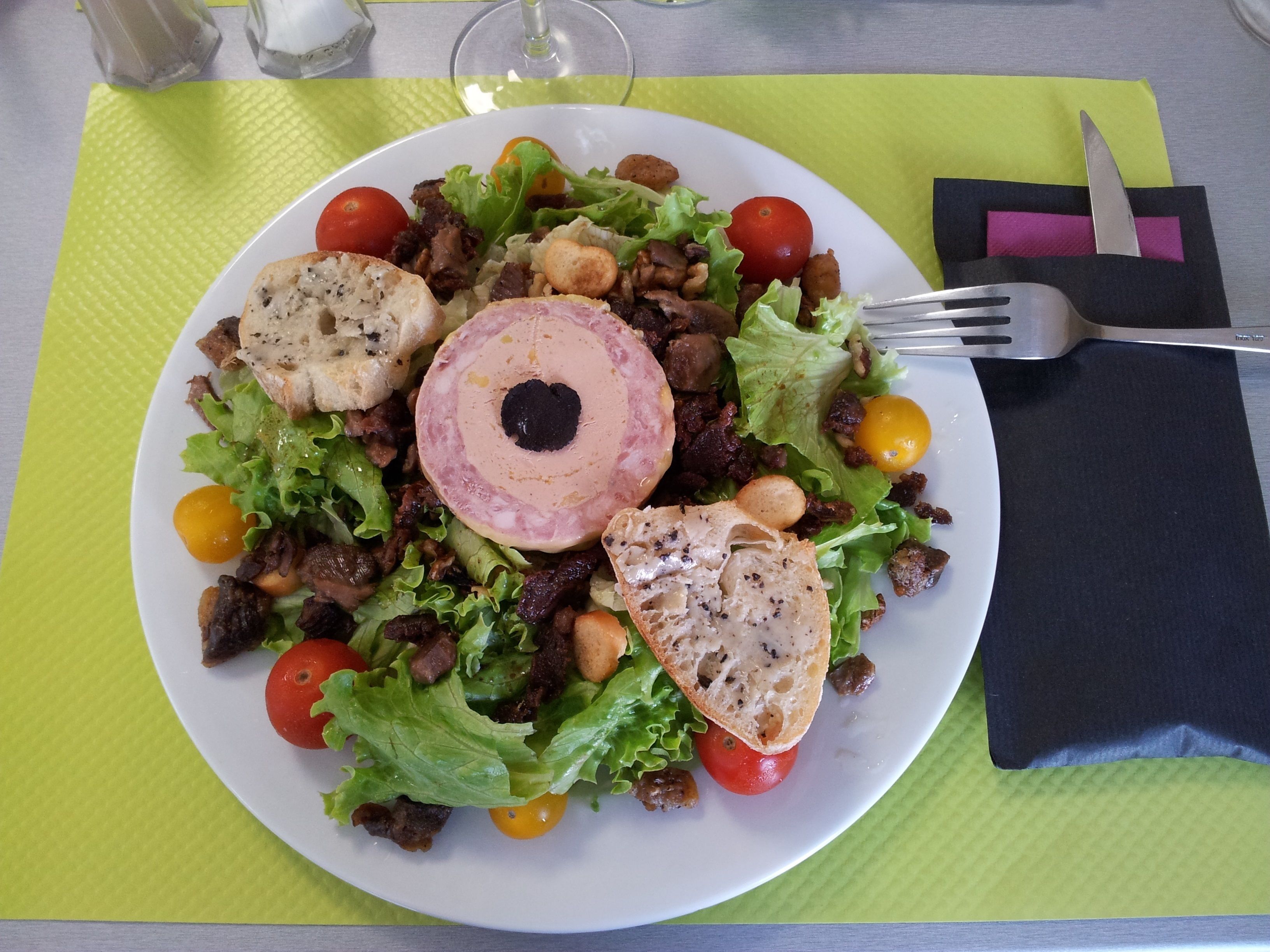 A plate of food with a variety of items including bread, meat, and vegetables, accompanied by a fork and a napkin on a green placemat.
