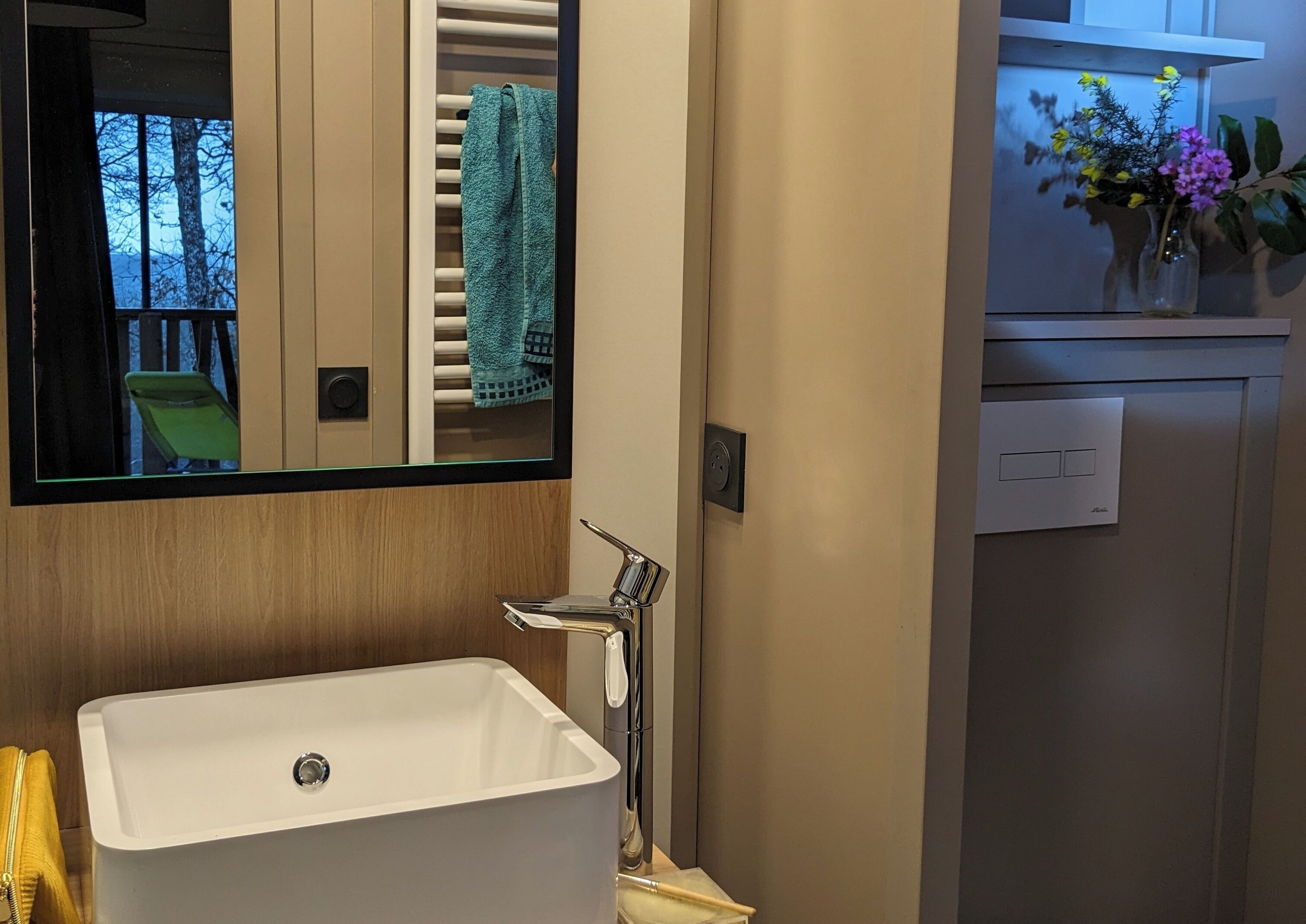 A bathroom with a white sink, a mirror, a towel rack, and a small window with a view of trees.