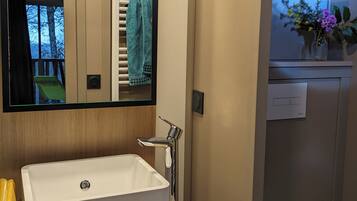 A bathroom with a white sink, a mirror, a towel rack, and a small window with a view of trees.