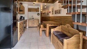 A compact kitchen with a refrigerator, wooden cabinets, a sink, and a dining area with a bench and table.