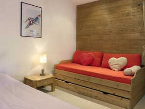 A bedroom with a wooden headboard, a red sofa with heart-shaped pillows, a bedside table with a lamp, and a framed poster on the wall.