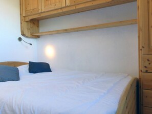 A wooden-framed bed with white bedding, a wall-mounted light, and a wooden cabinet above the bed.