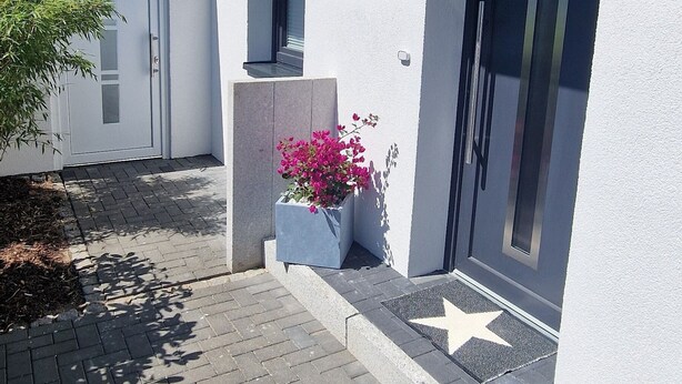 Un edificio moderno con fachada blanca, una puerta oscura y un felpudo con forma de estrella.