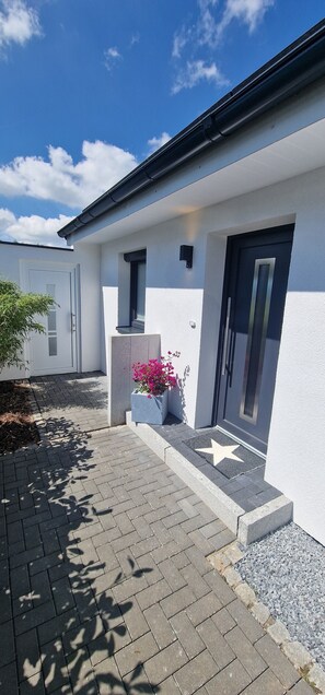 A modern building with a white facade, a dark door, and a star-shaped doormat. - Haus Lena 2 - Vacation near the Baltic Sea - Now with e-charging station! (Pansdorf)