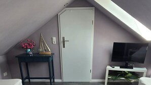 Un dormitorio tipo loft moderno con techo inclinado, un ventanal grande, un televisor de pantalla plana, un escritorio pequeño y una planta decorativa.