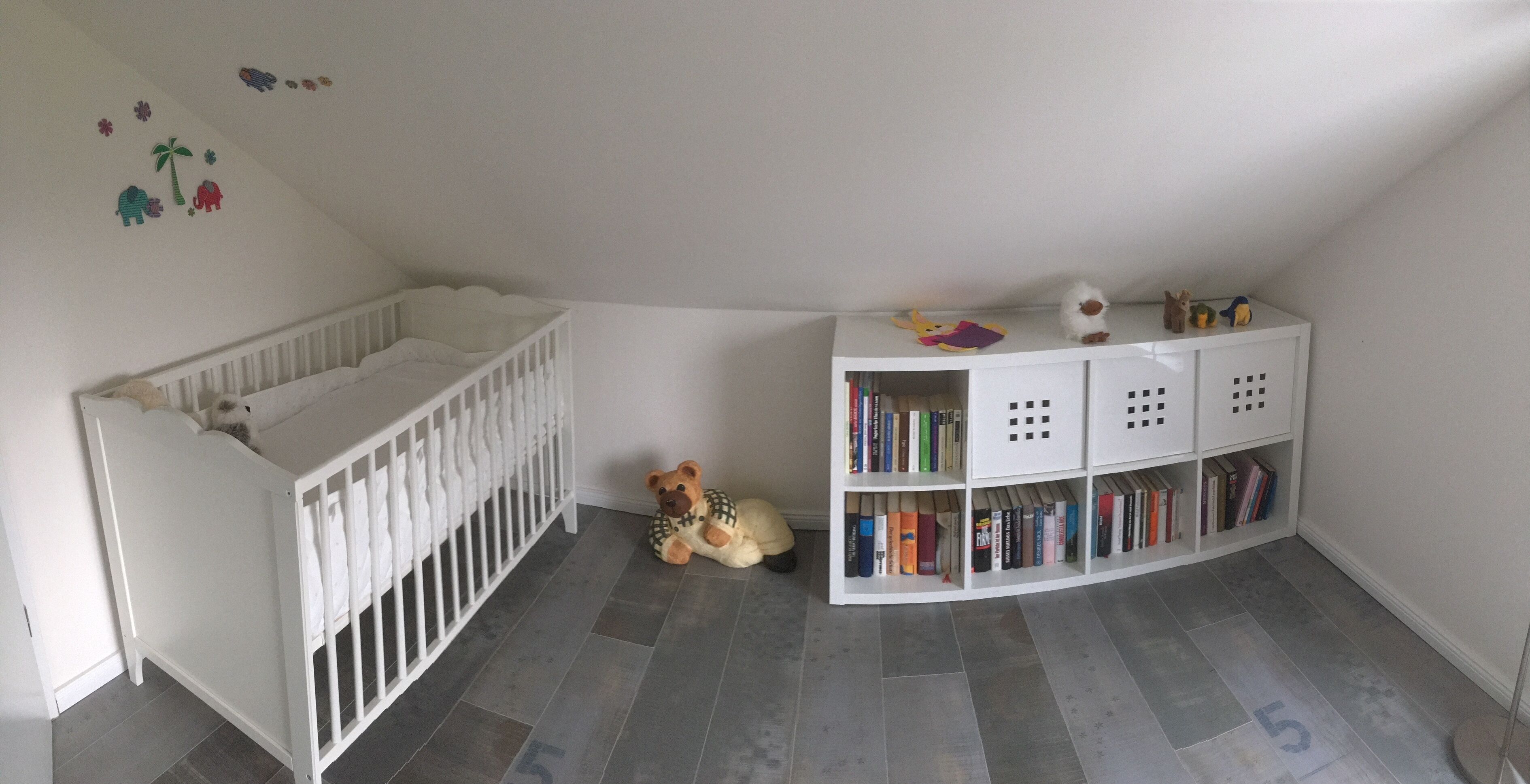 Een kamer met een wit wiegje, een boekenkast en een teddybeer.