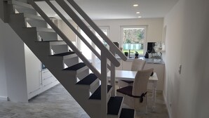 Una cocina moderna con armarios blancos, un comedor con sillas de mimbre y una escalera que sube a otro nivel.