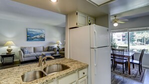 A kitchen with a double sink, white cabinets, and a refrigerator. There is a dining area with a table and chairs visible through a glass door.