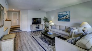 A living room with a sofa, a coffee table, a TV, and a painting on the wall.