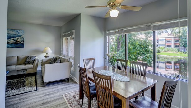 A dining area with a table, chairs, a ceiling fan, and a view of greenery outside.