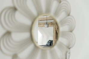 A circular mirror reflecting a room with a wooden ceiling, a hanging light fixture, and a bed with pillows.