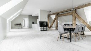A spacious loft with a dining area featuring a wooden table and chairs, a television, and a kitchen in the background. - Majestic 300m2 Apartment (Copenhagen)