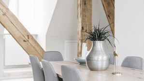 A dining table with a vase of green plants, grey chairs, and a wooden beam structure in the background. - Majestic 300m2 Apartment (Copenhagen)
