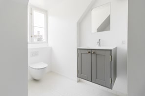 A modern bathroom with a white toilet, grey cabinets, a large mirror, and a window.