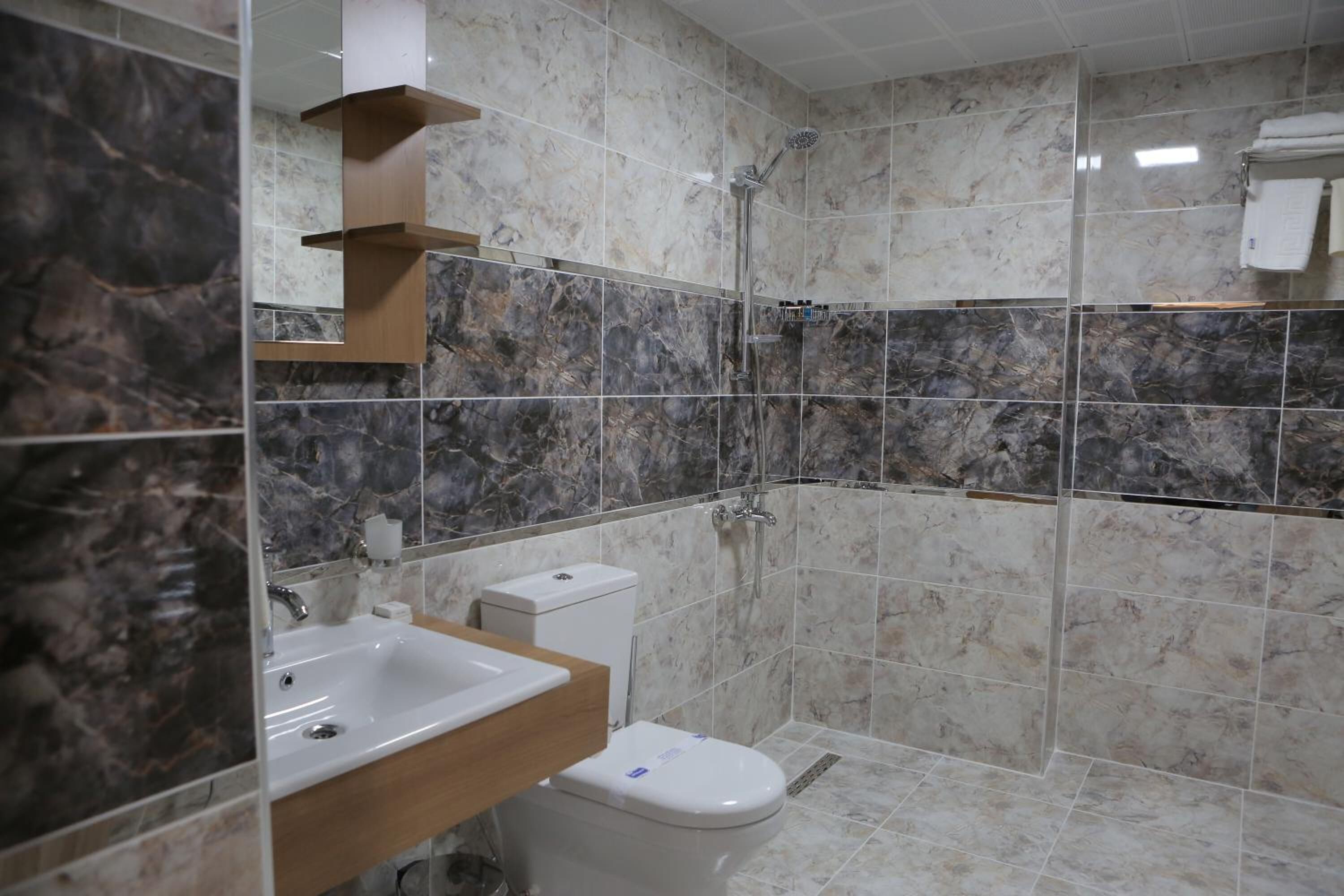 A bathroom with a marble-tiled shower, a white sink, and a toilet.