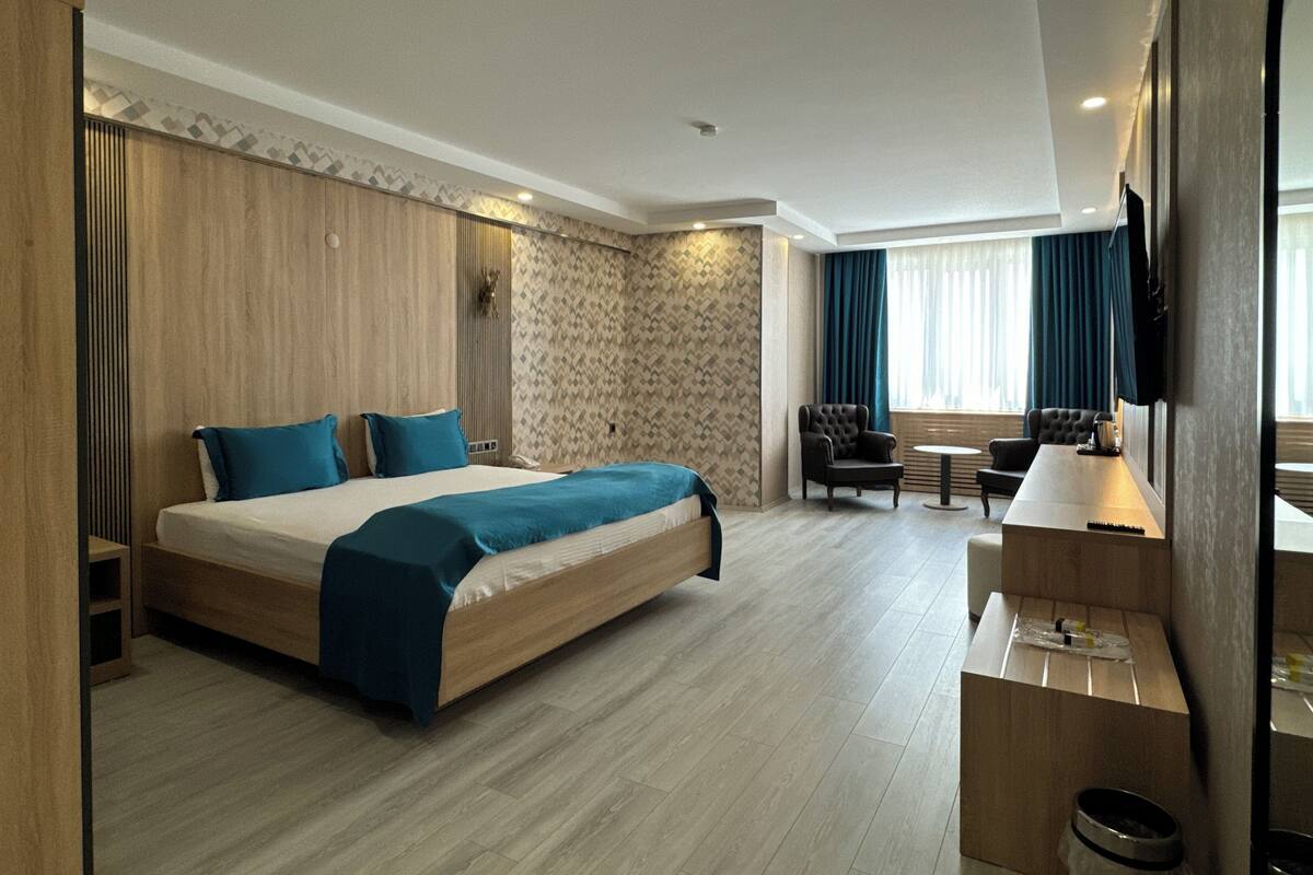 A modern hotel room with a large bed, a seating area with a table and chairs, and a TV mounted on the wall.