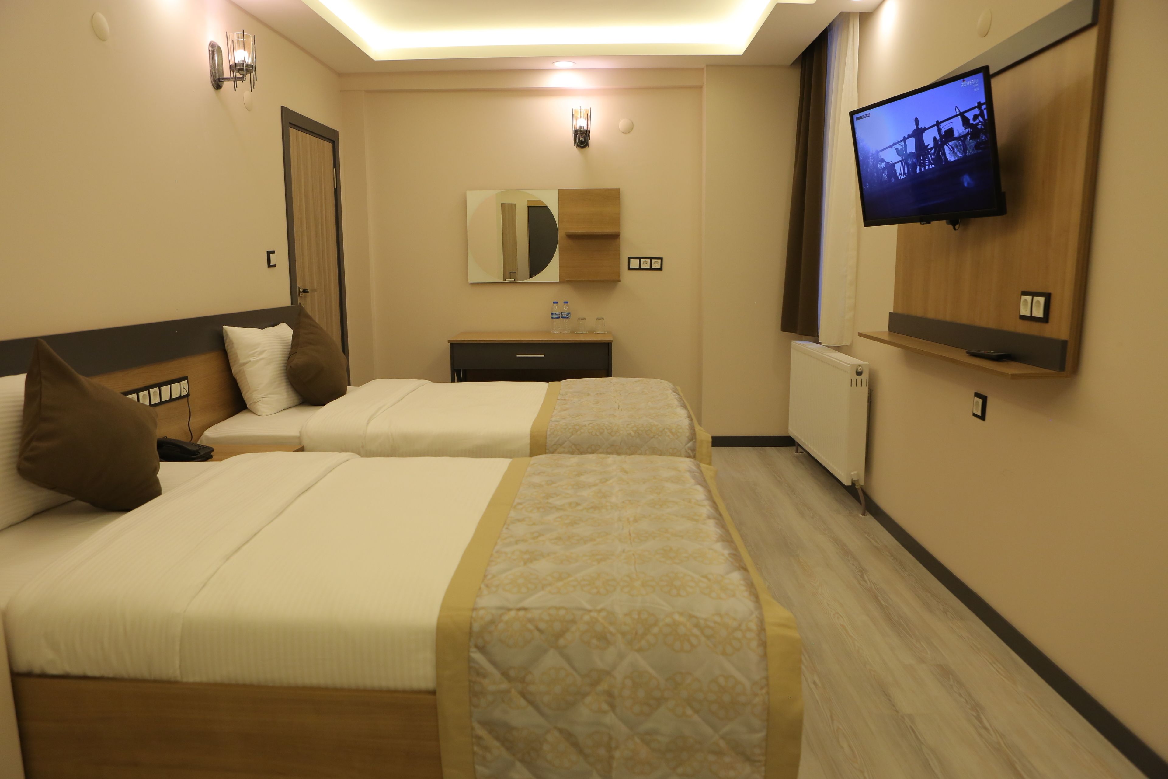 A hotel room with two beds, a TV, a mirror, and a small desk.