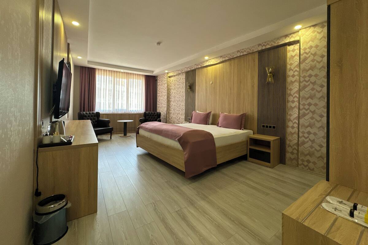 A modern hotel room with a large bed, a desk with a TV, and a small seating area.