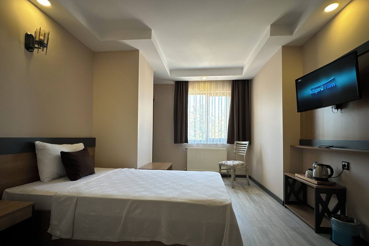 A hotel room with a large bed, a television mounted on the wall, a small table with a kettle, and a chair.