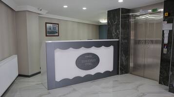 A reception area with a marble floor, a reception desk, a framed picture on the wall, and an elevator.