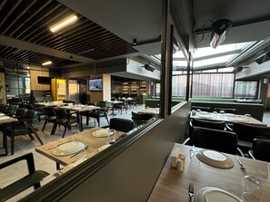 A modern restaurant with multiple dining areas, including booths and tables, and a television screen mounted on the wall. - Korkmaz Otel (Merzifon)