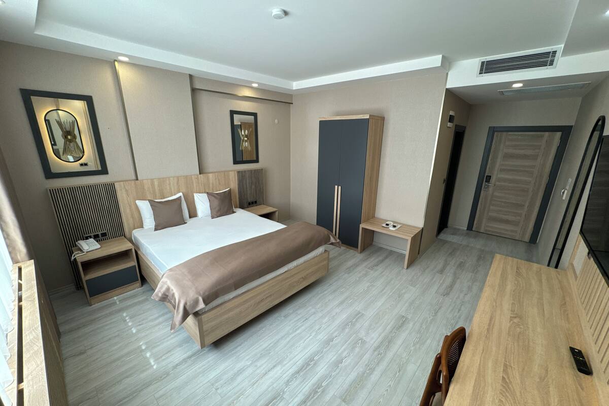 A modern hotel room with a large bed, bedside tables, a wardrobe, and a desk with a chair.