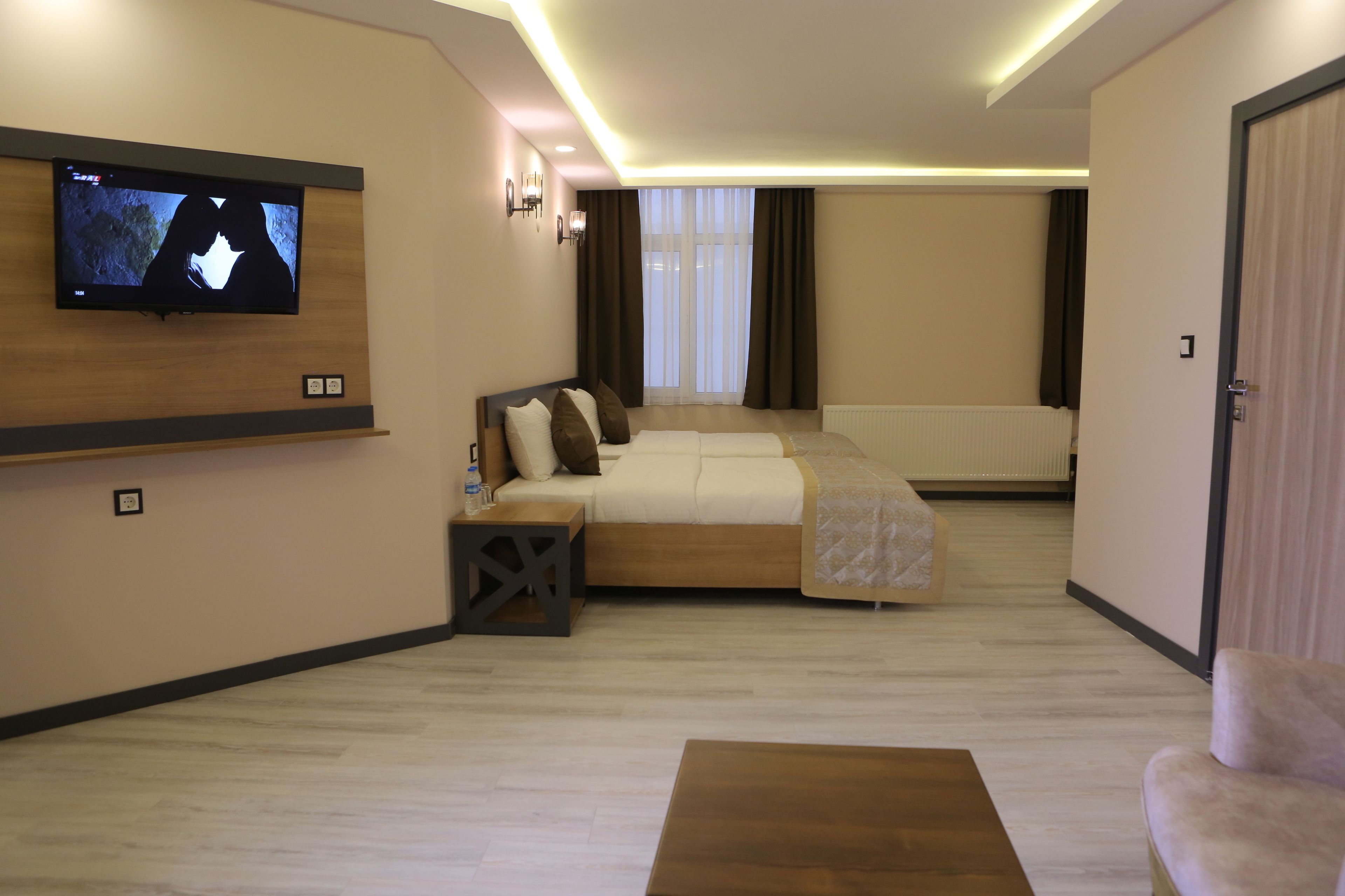 A modern hotel room with a large bed, a flat-screen TV mounted on the wall, and a wooden coffee table.