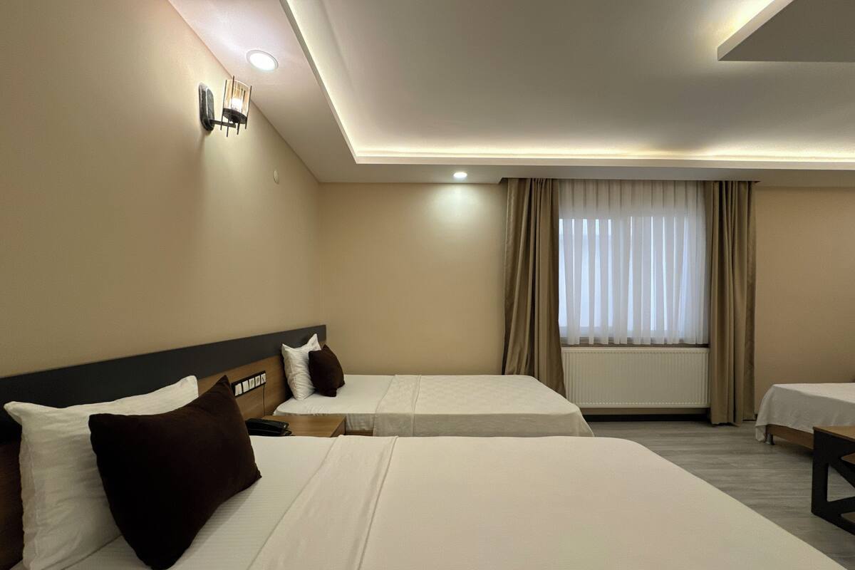 A hotel room with two beds, a nightstand, a lamp, and a window with curtains.
