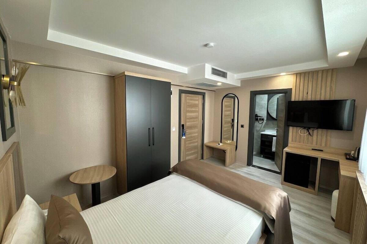A modern hotel room with a bed, a TV, a desk, and a mirror.