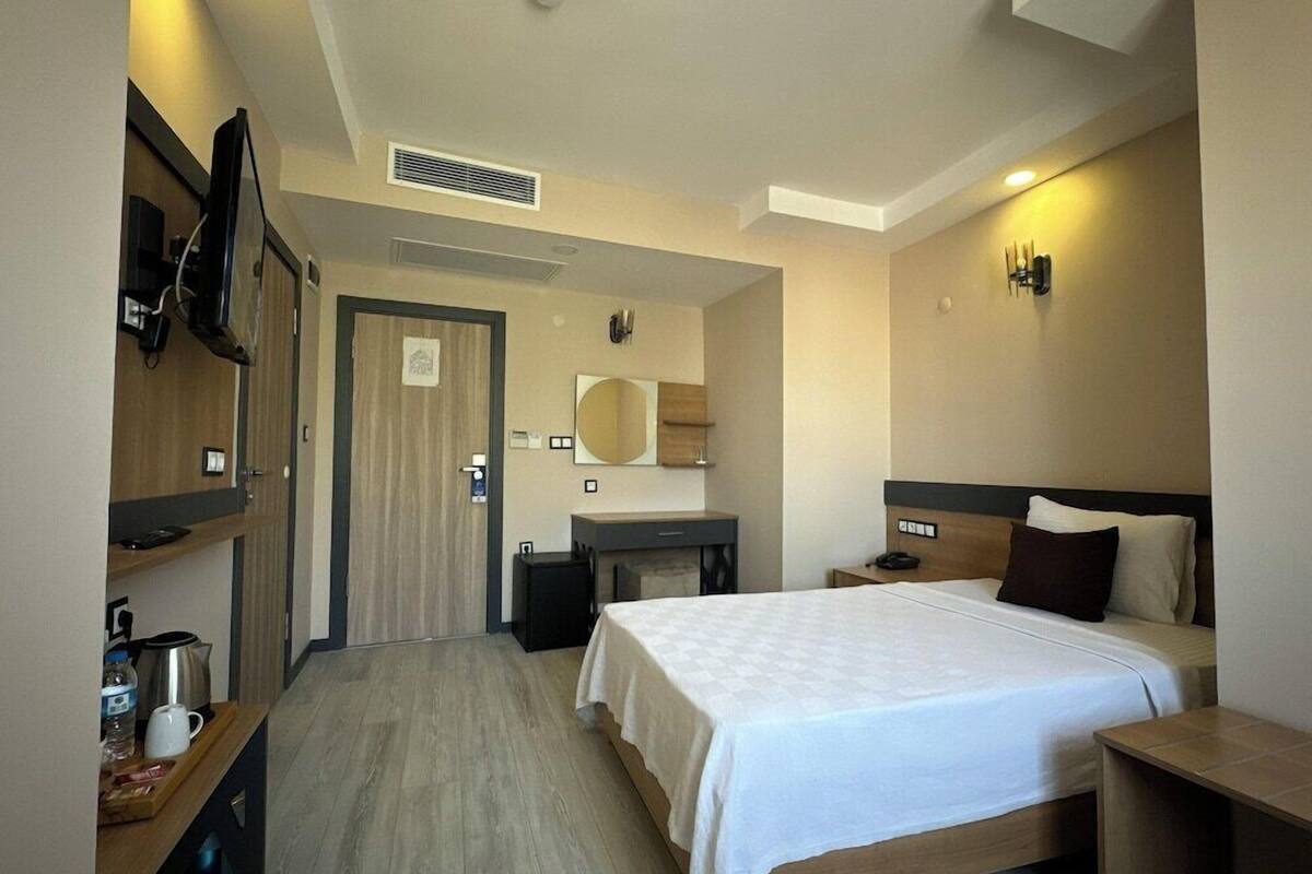 A hotel room with a bed, bedside tables, a desk, a mirror, a TV, and a wardrobe.