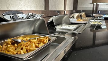 A buffet setup with various food items in metal containers, including fried potatoes and eggs, in a modern hotel setting.