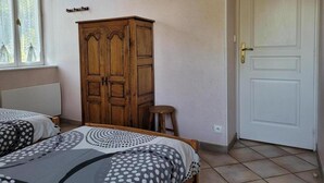 Un dormitorio con dos camas, un armario de madera, una puerta blanca y una ventana con cortinas de encaje.