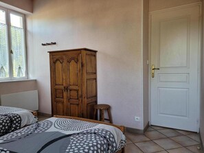 A bedroom with two beds, a wooden wardrobe, a white door, and a window with lace curtains. - 2-bedroom house with enclosed garden in Sologne, pets allowed (Aurouer)