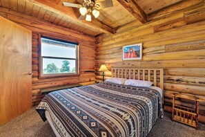 Un dormitorio tipo cabaña de troncos con una cama, una ventana, una lámpara y un cuadro en la pared.