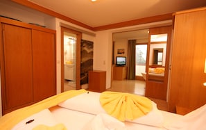 A hotel room with a bed, a TV, wooden furniture, and a view of the outdoors. - Hotel Appartement Hochkönig (Ramsau am Dachstein)