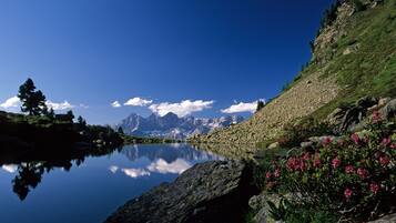 A serene lake with mountains in the background, surrounded by rocky terrain and greenery.