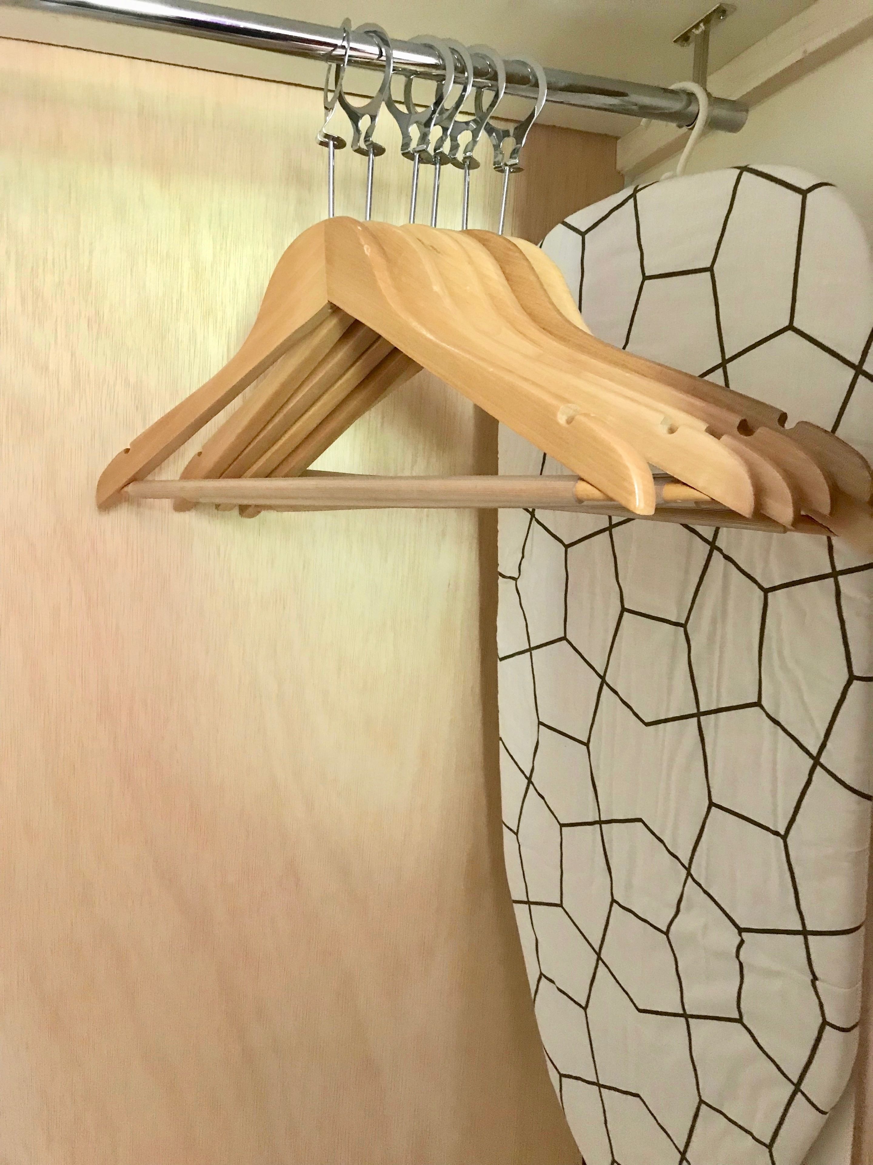 A wooden hanger rack with multiple hangers against a wall with a geometric-patterned curtain.