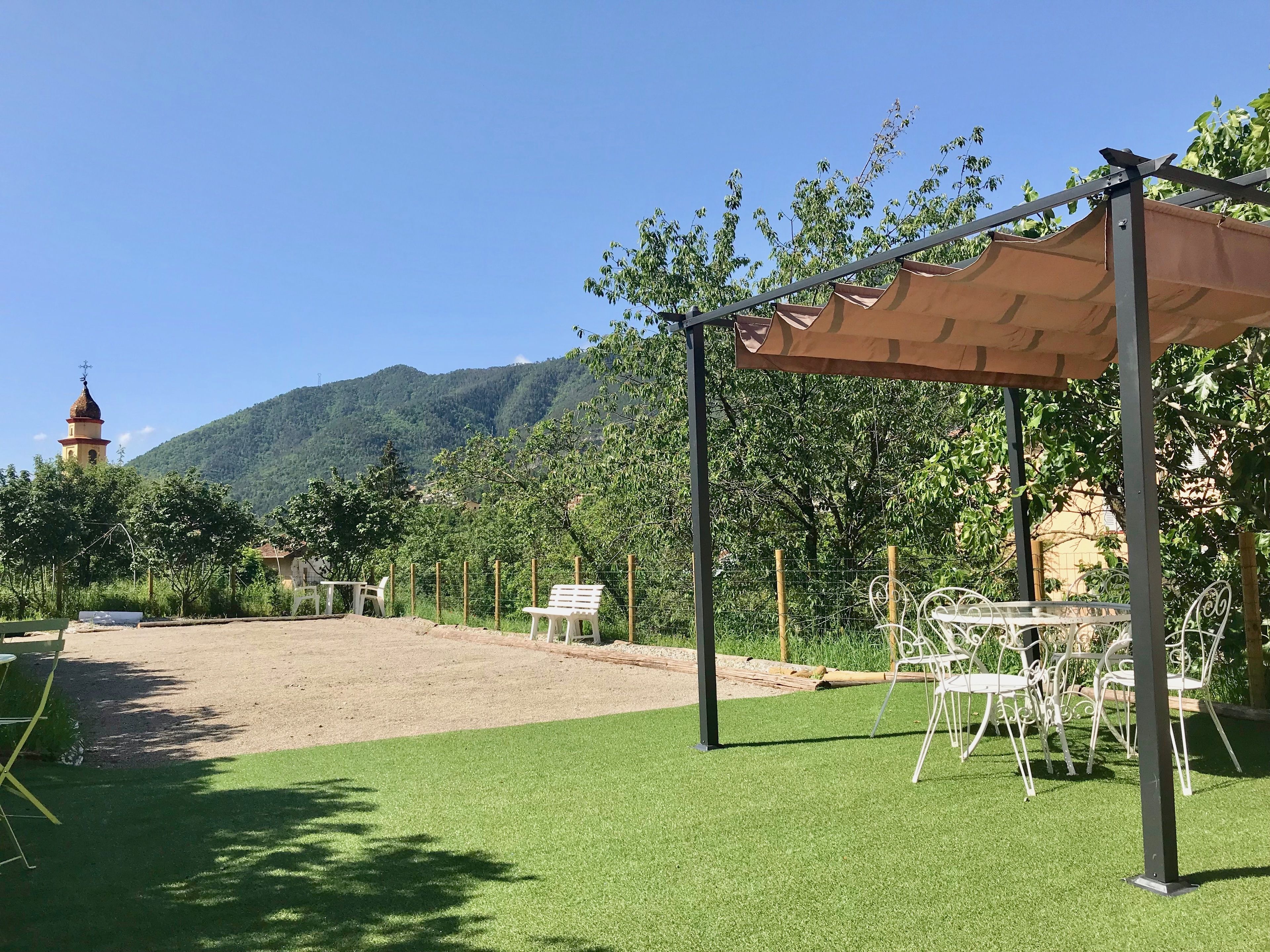 Un espacio al aire libre con césped artificial, una pérgola y sillas de metal blanco.