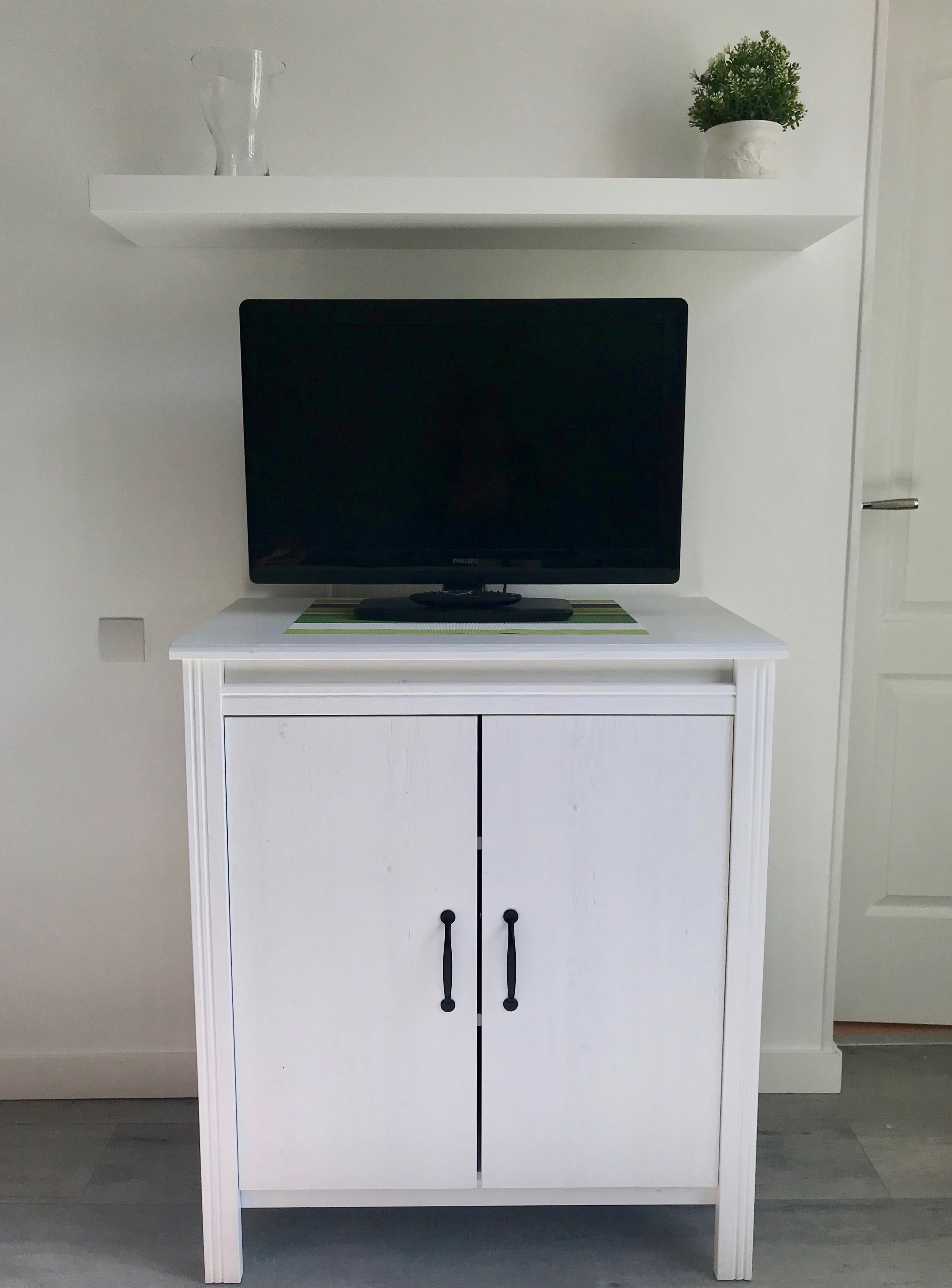 Een witte kast met een flatscreen-televisie erboven, een klein plantje op het plankje en een deur met twee handgrepen.