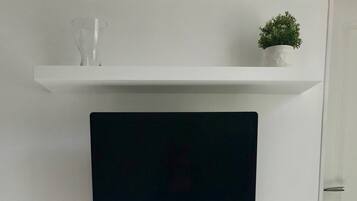 Een witte kast met een flatscreen-televisie erboven, een klein plantje op het plankje en een deur met twee handgrepen.