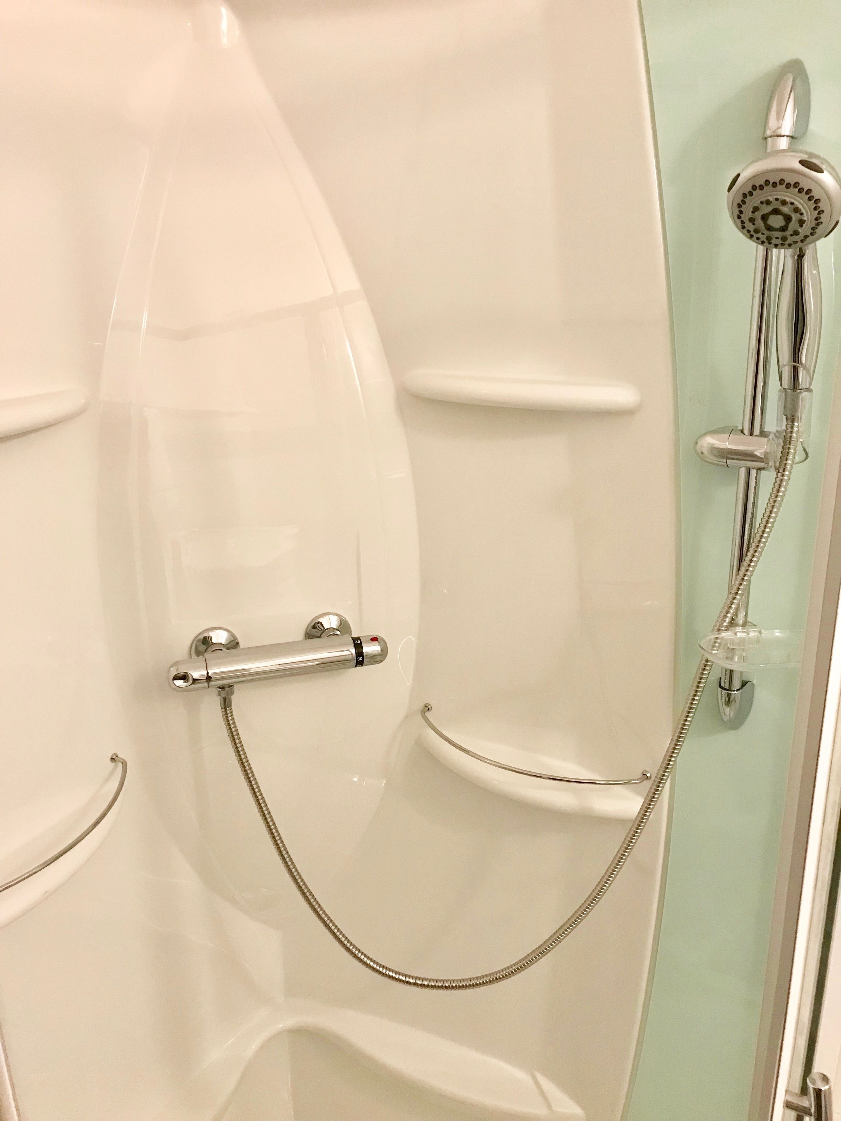 Un baño con cabina de ducha de vidrio, cabezal de ducha manual y manguera de ducha.