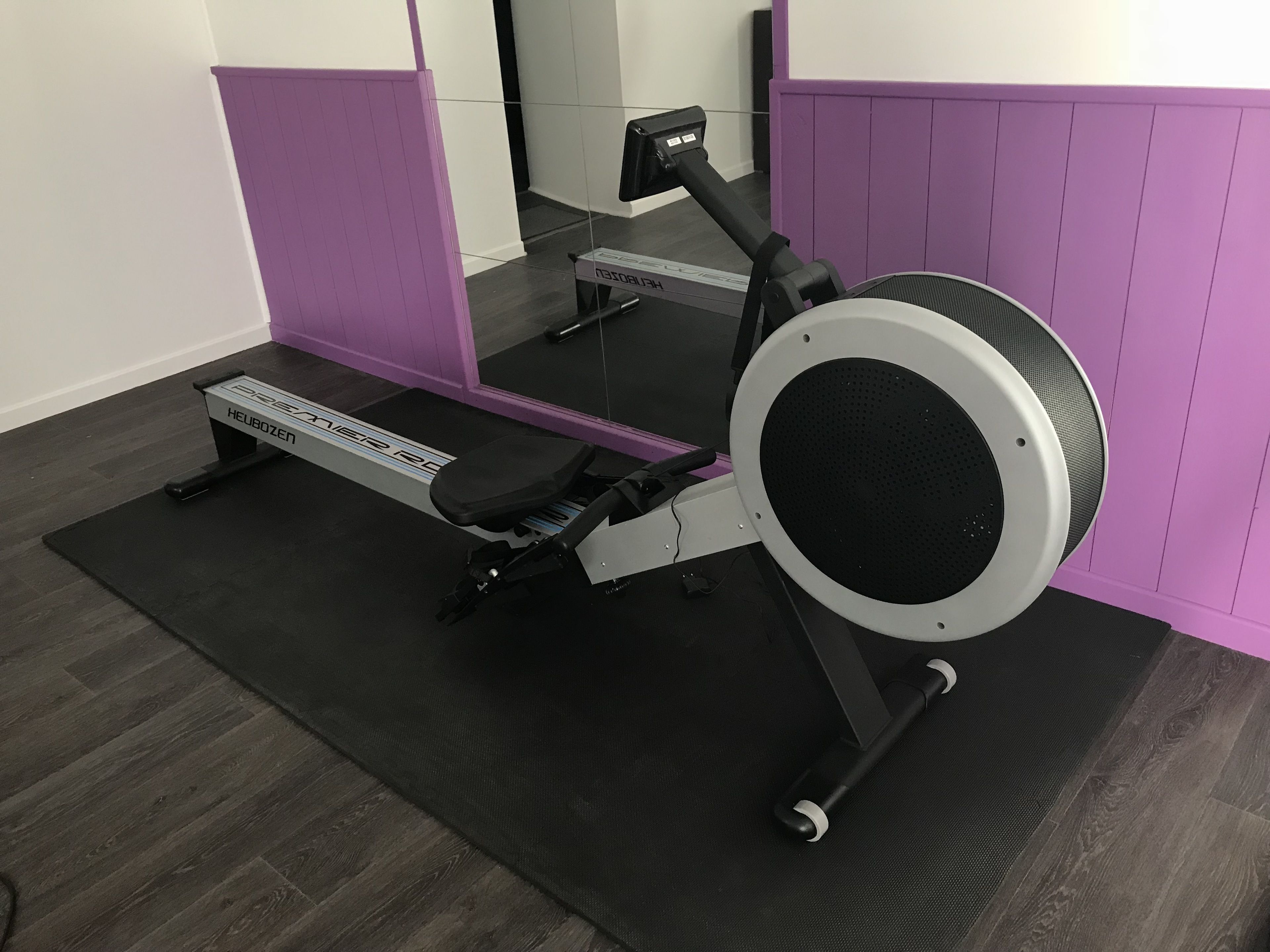 A stationary bike with a digital display, positioned in a room with purple walls and a wooden floor.