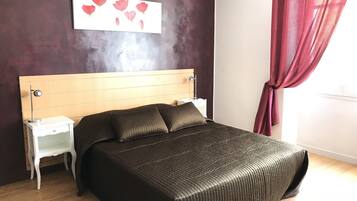 A bedroom with a wooden headboard, a bed with a dark quilted bedspread, a nightstand with a lamp, and a wall art piece above the bed.