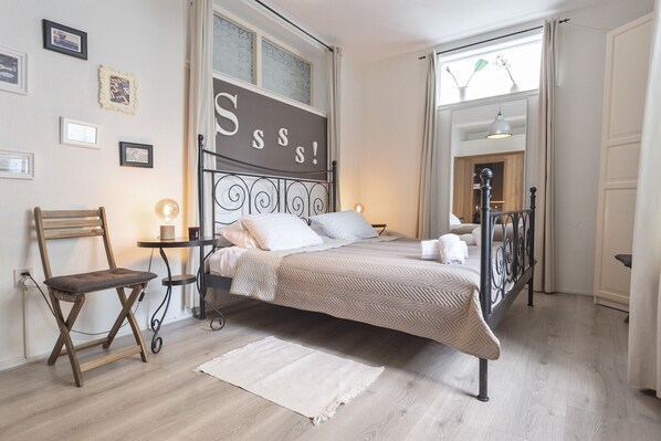 A bedroom with a bed, a chair, a bedside table, and a wall with framed pictures.