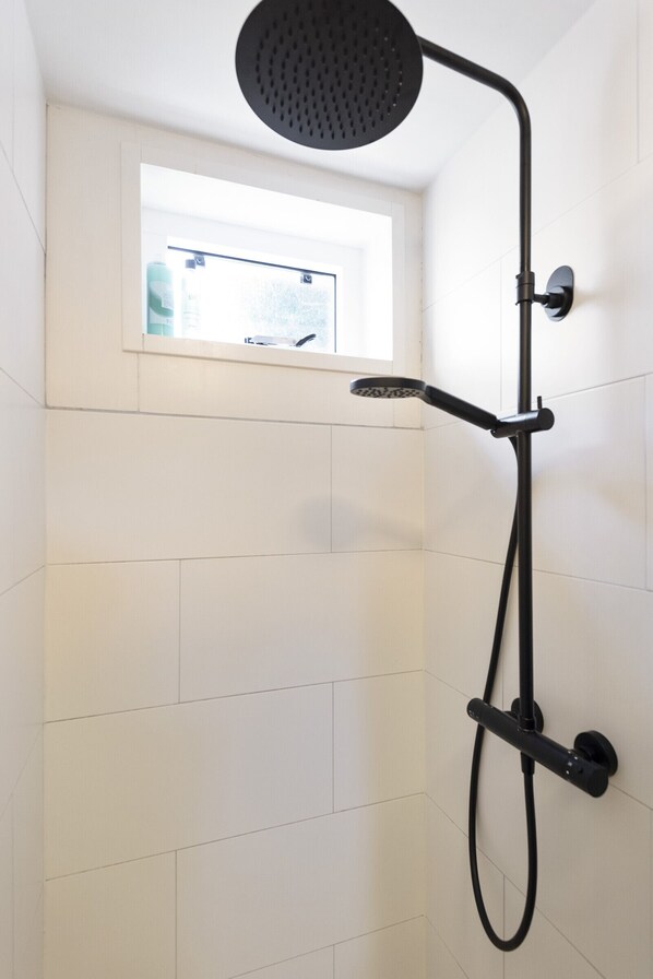 Ducha con cabezal de ducha de mano y cabezal fijo, montada en una pared con azulejos blancos.