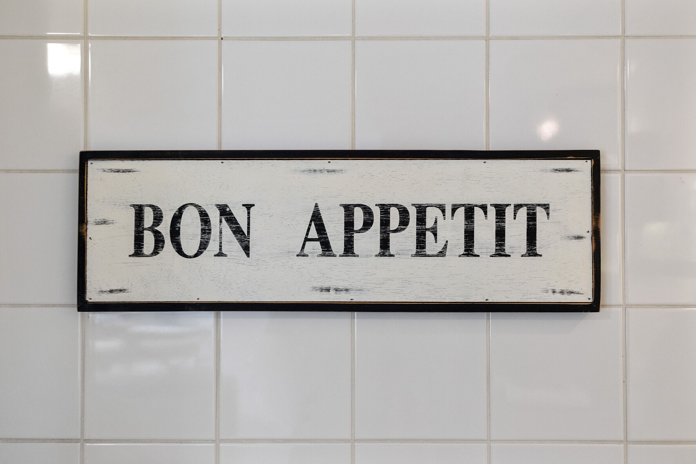 Ein Schild mit dem Schriftzug 'BON APPETIT' an einer gefliesten Wand.