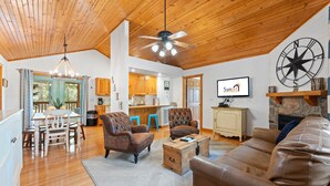 A spacious living room with a wooden ceiling, a fireplace, and a television displaying 'Sunset Realty'. - 2BR lodge at Stonebridge Resort near Silver Dollar City. (Branson West)