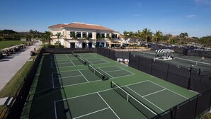 A tennis court with multiple courts, a clubhouse, and a parking area with golf carts. - Pristine Home in Golf Community 3 Bedroom/3.5 Bathroom (West Palm Beach)