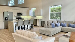 A spacious living area with a modern kitchen, a large window, and a seating arrangement. - Pristine Home in Golf Community 3 Bedroom/3.5 Bathroom (West Palm Beach)