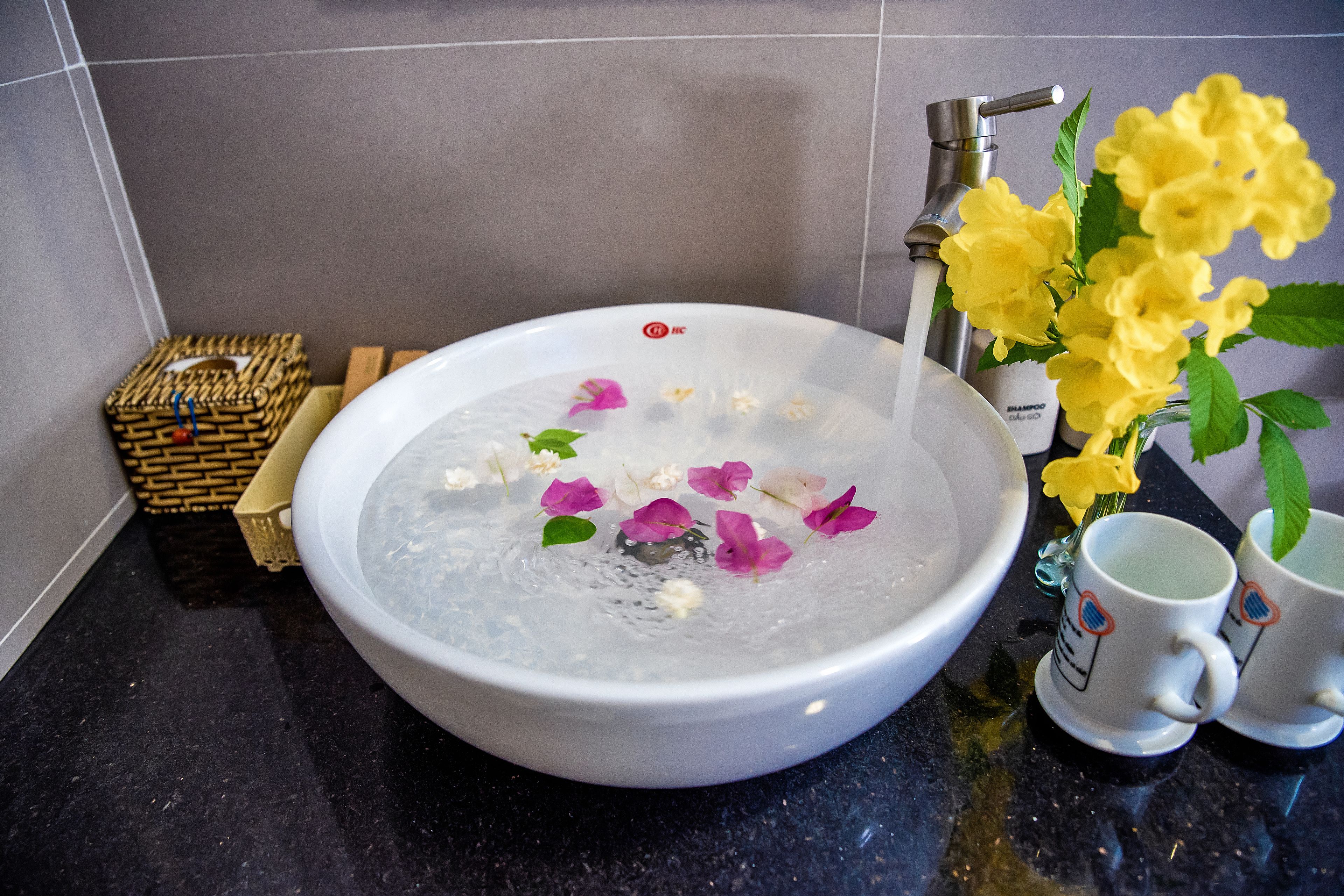 A bathroom sink with water, flowers, and a bottle of shampoo.